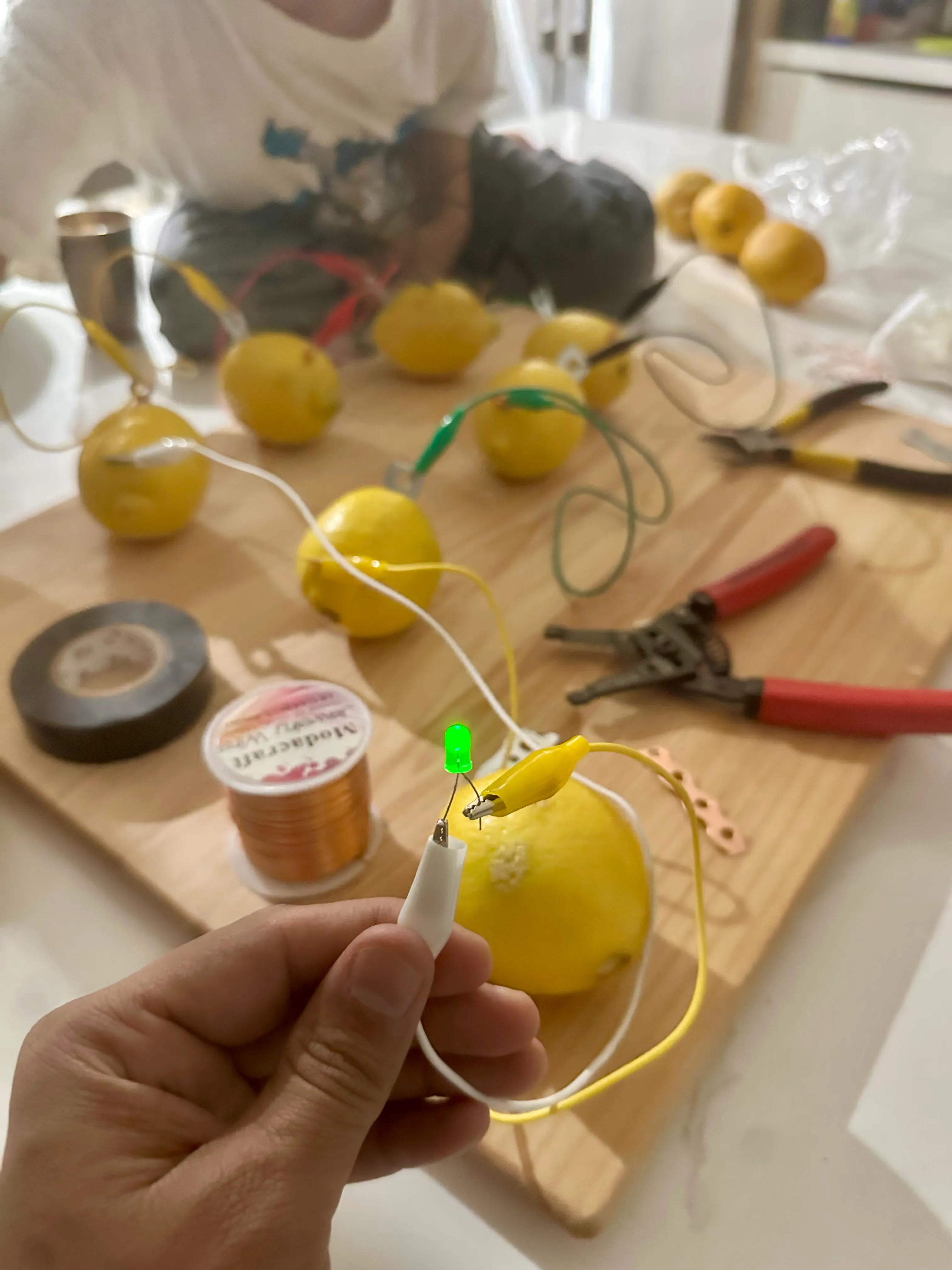 Close-up of a glowing green LED clipped between a lemon and a white alligator lead